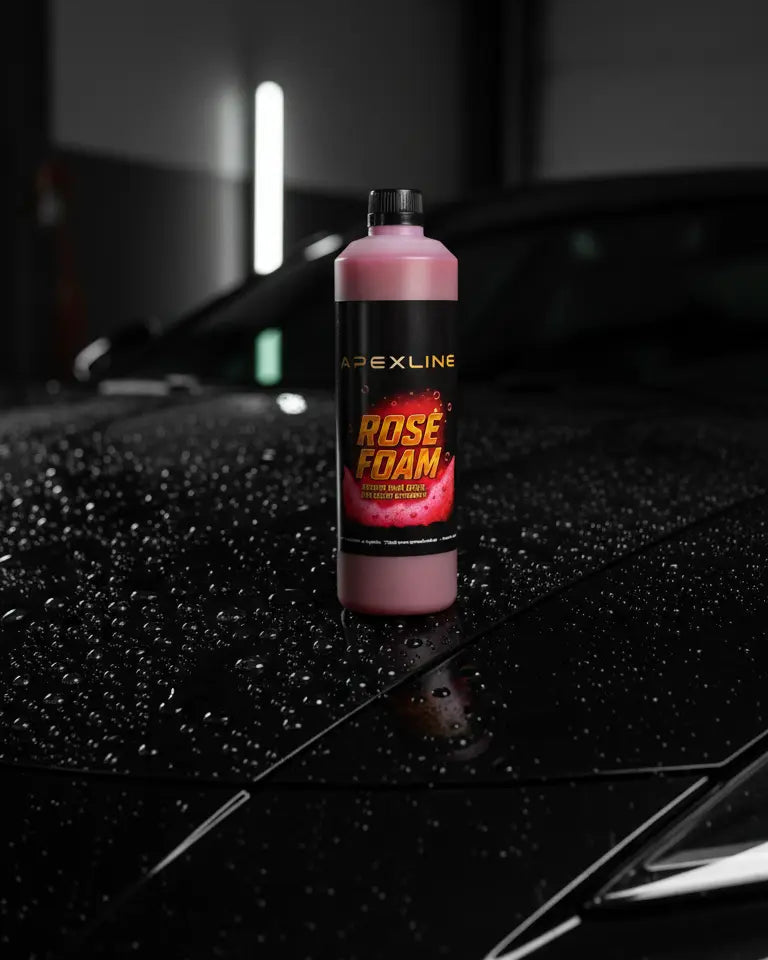 Foto con capó de coche negro mojado de fondo y champú para coche con agente espumante de color rosa en el centro. Botella de champú rosa para coche PH neutro de alta tecnología.