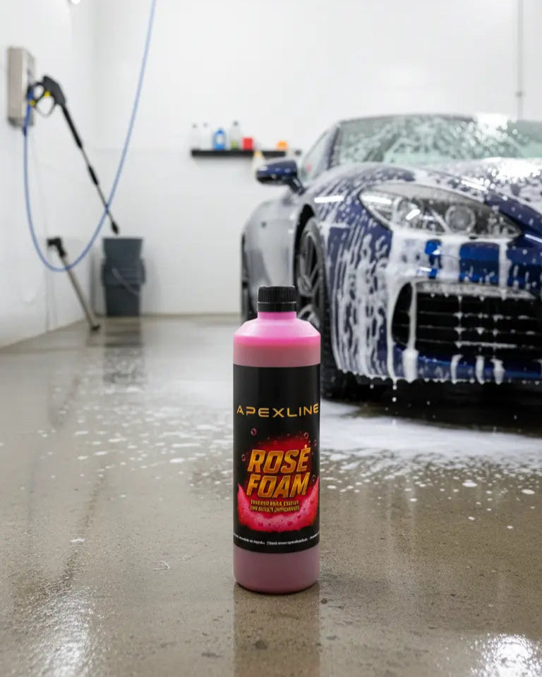 Foto con fondo con coche limpiándose y champú para coche con agente espumante de color rosa en el centro. Botella de champú rosa para coche PH neutro de alta tecnología.