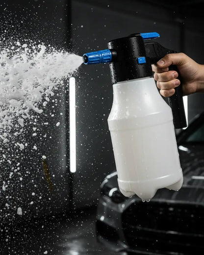 Foto con fondo negro de workshop y espumador foamer en el centro siendo usado por una mano de persona. Espumador a batería con cargador incluido de 1.5L de capacidad.