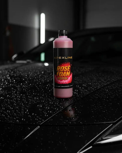 Foto con capó de coche negro mojado de fondo y champú para coche con agente espumante de color rosa en el centro. Botella de champú rosa para coche PH neutro de alta tecnología. 